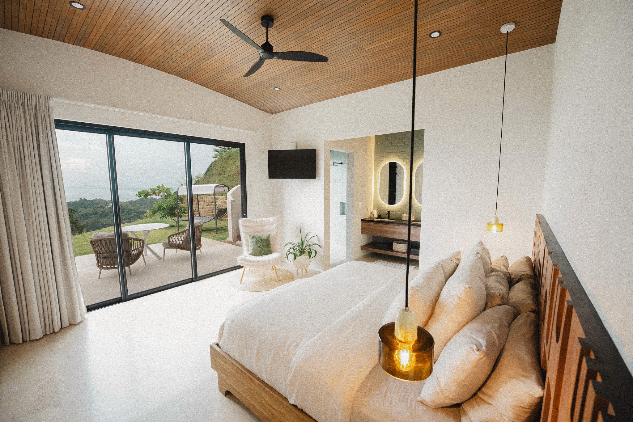 Luxury bedroom suite with a wood-paneled ceiling, ensuite bathroom access, and sliding glass doors opening to a private terrace with ocean views.