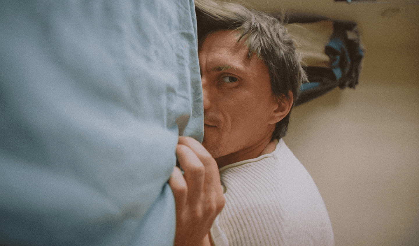 Person partially concealed behind fabric in an intimate domestic setting.