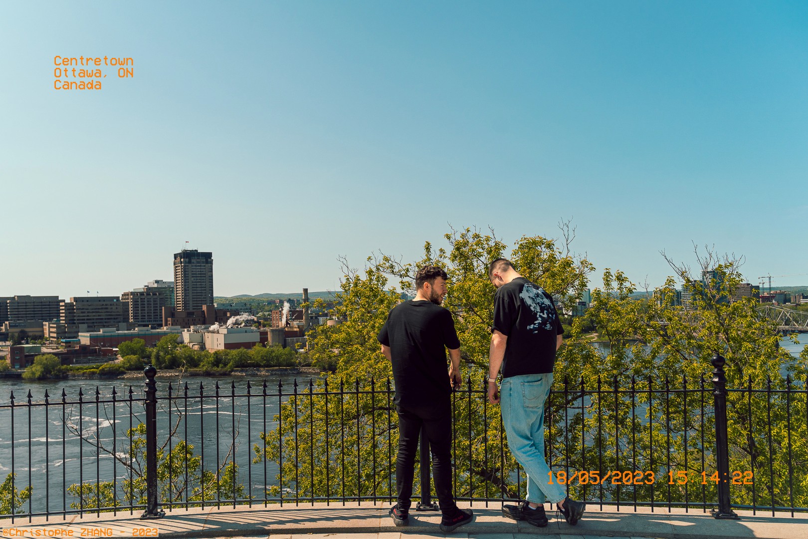 Point de vue panoramique sur Gatineau avec deux personnes se tenant près d’une clôture, sous un ciel dégagé.