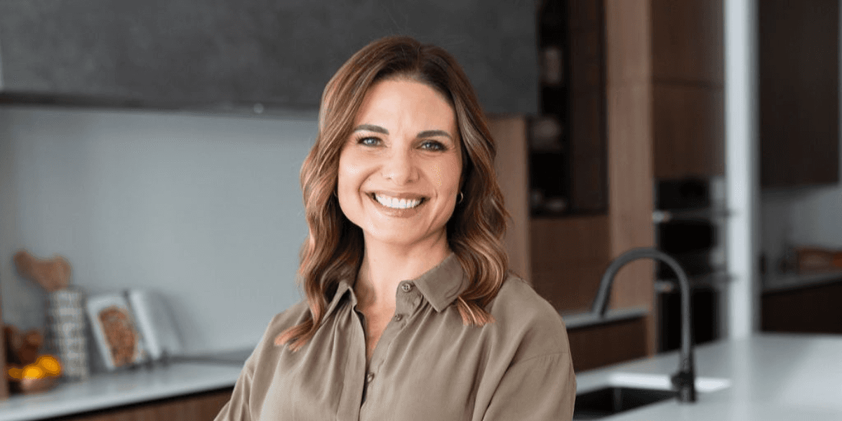 Angela Porrelli smiling in a modern kitchen wearing an olive green blouse.