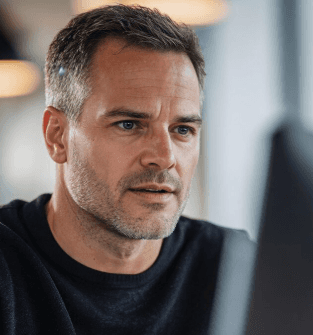 Confident woman with long curly hair wearing sunglasses and a shimmering top, photographed from a low angle against a deep blue sky.