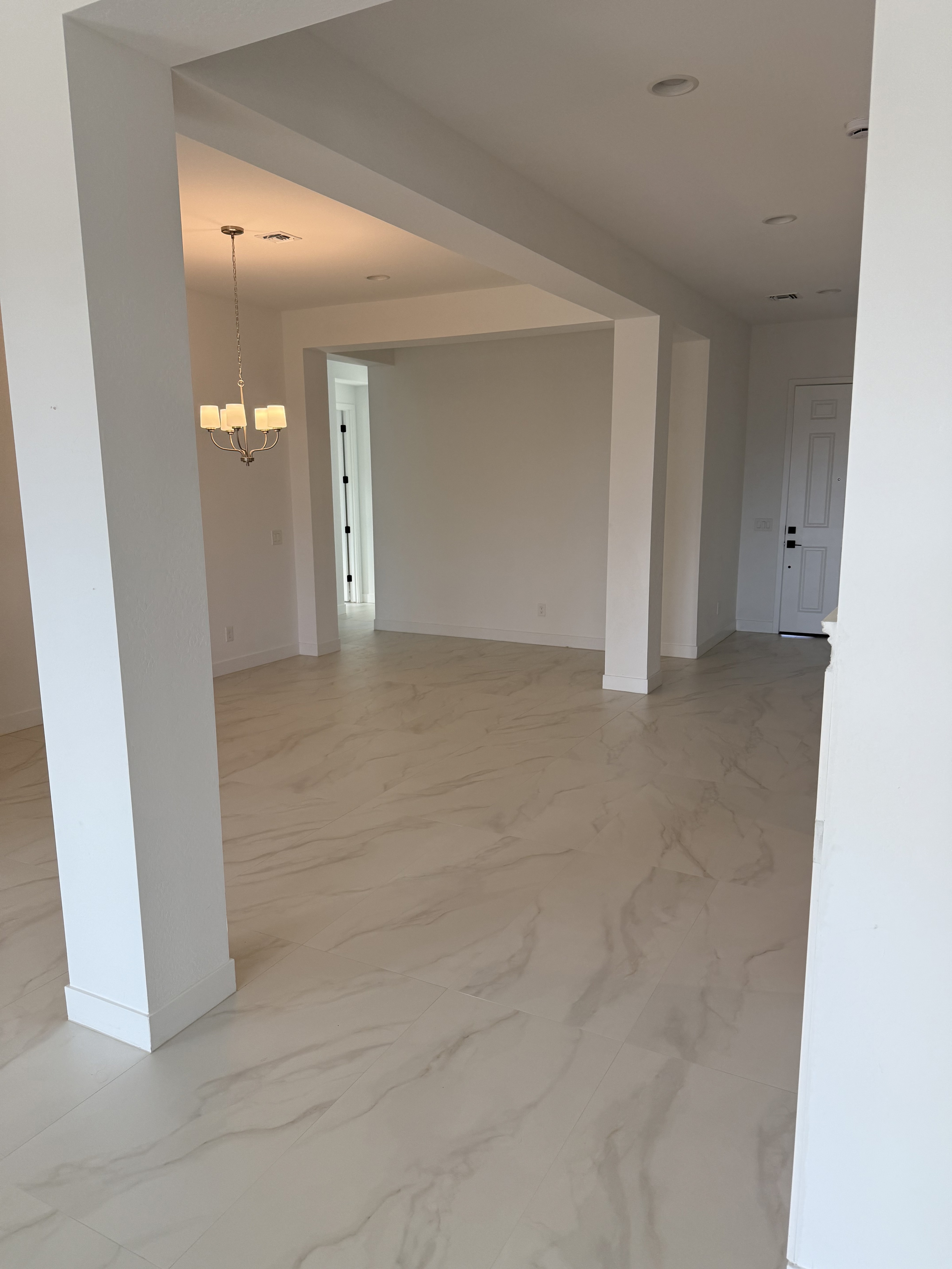 Modern open-plan living area with gray wood-look tile flooring, kitchen island, and pendant lights in a new home under construction.
