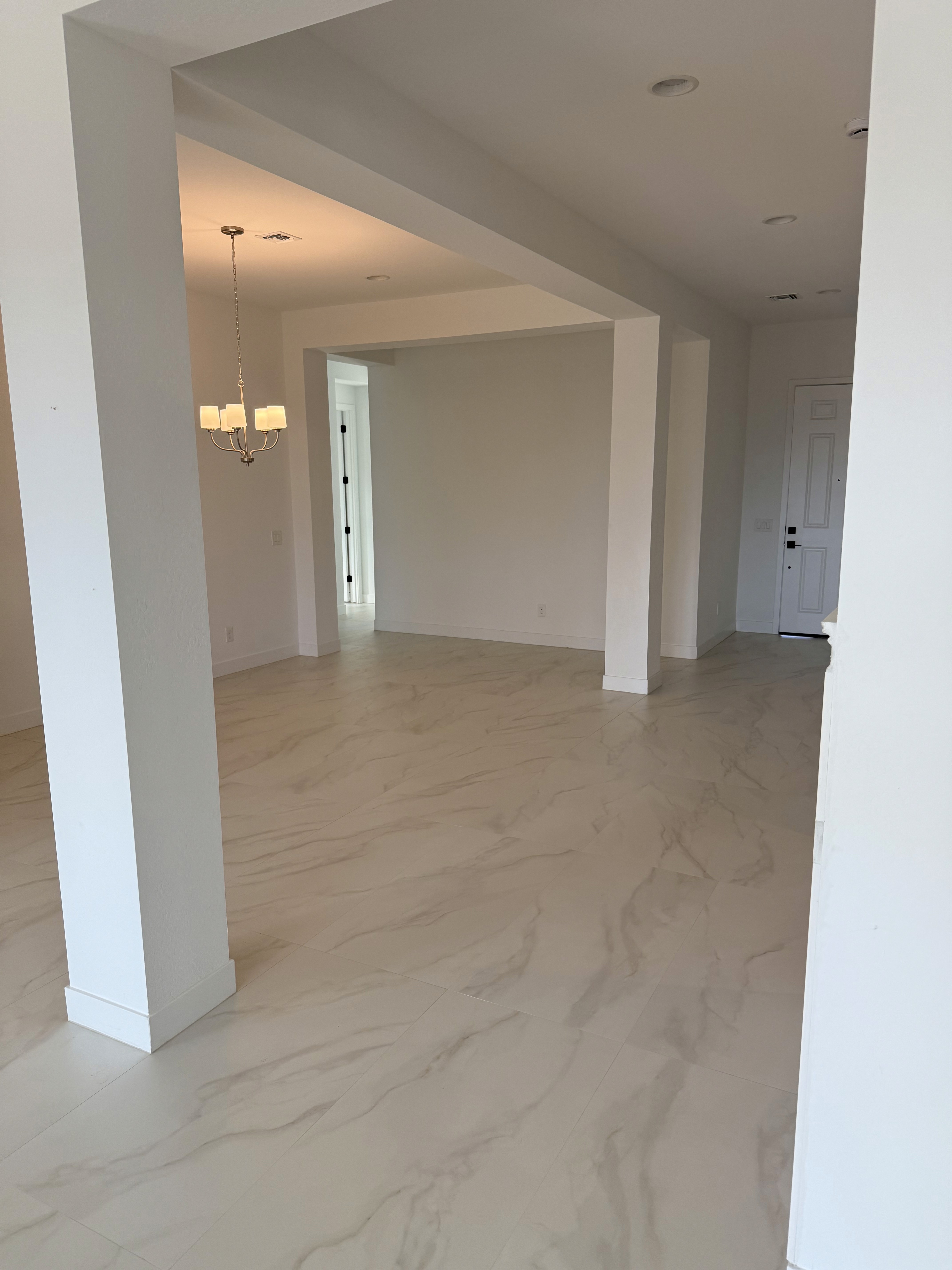 Modern open-plan living area with gray wood-look tile flooring, kitchen island, and pendant lights in a new home under construction.