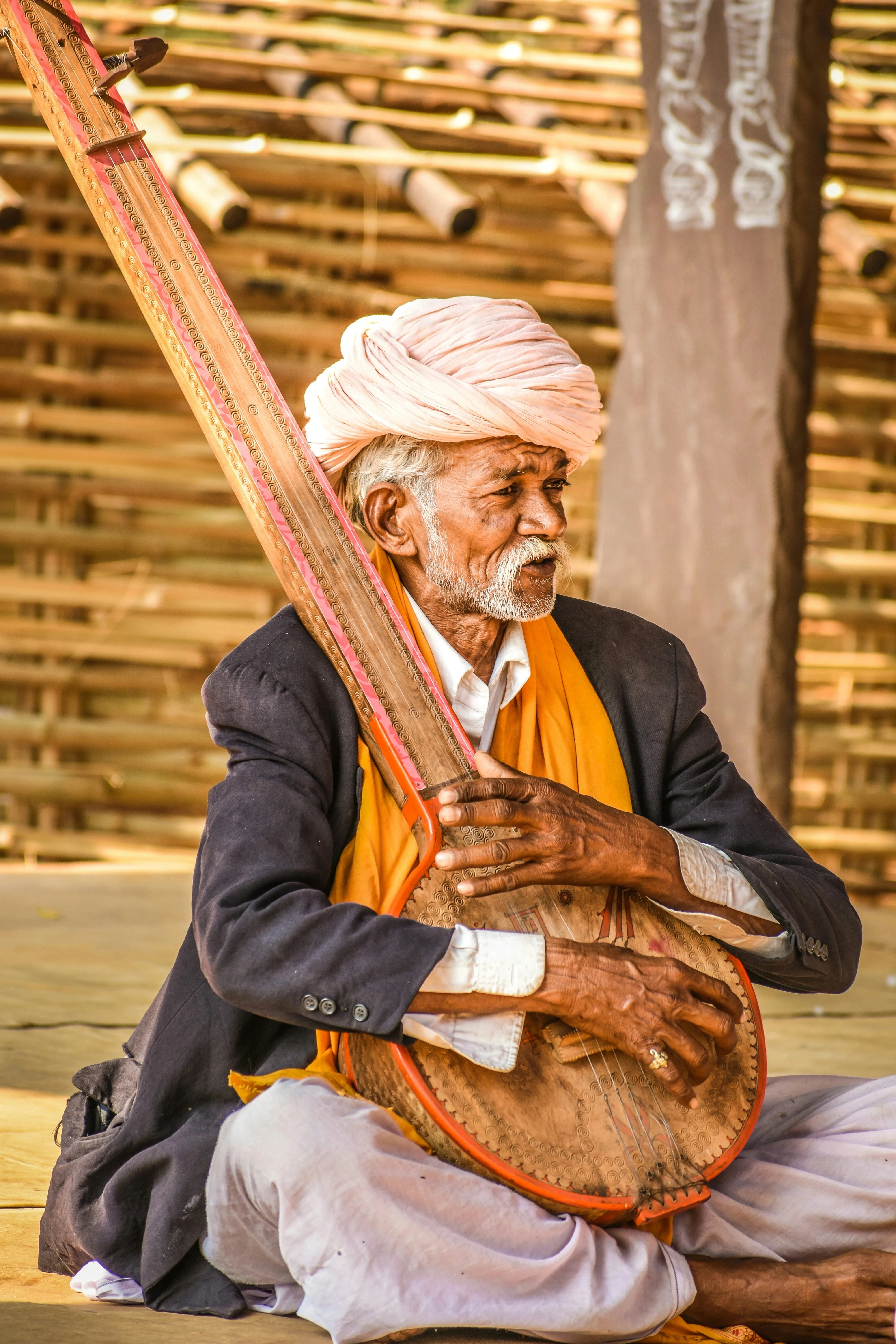 An old indian male srtist with a traditional turban holding a musical instrument close to his heart