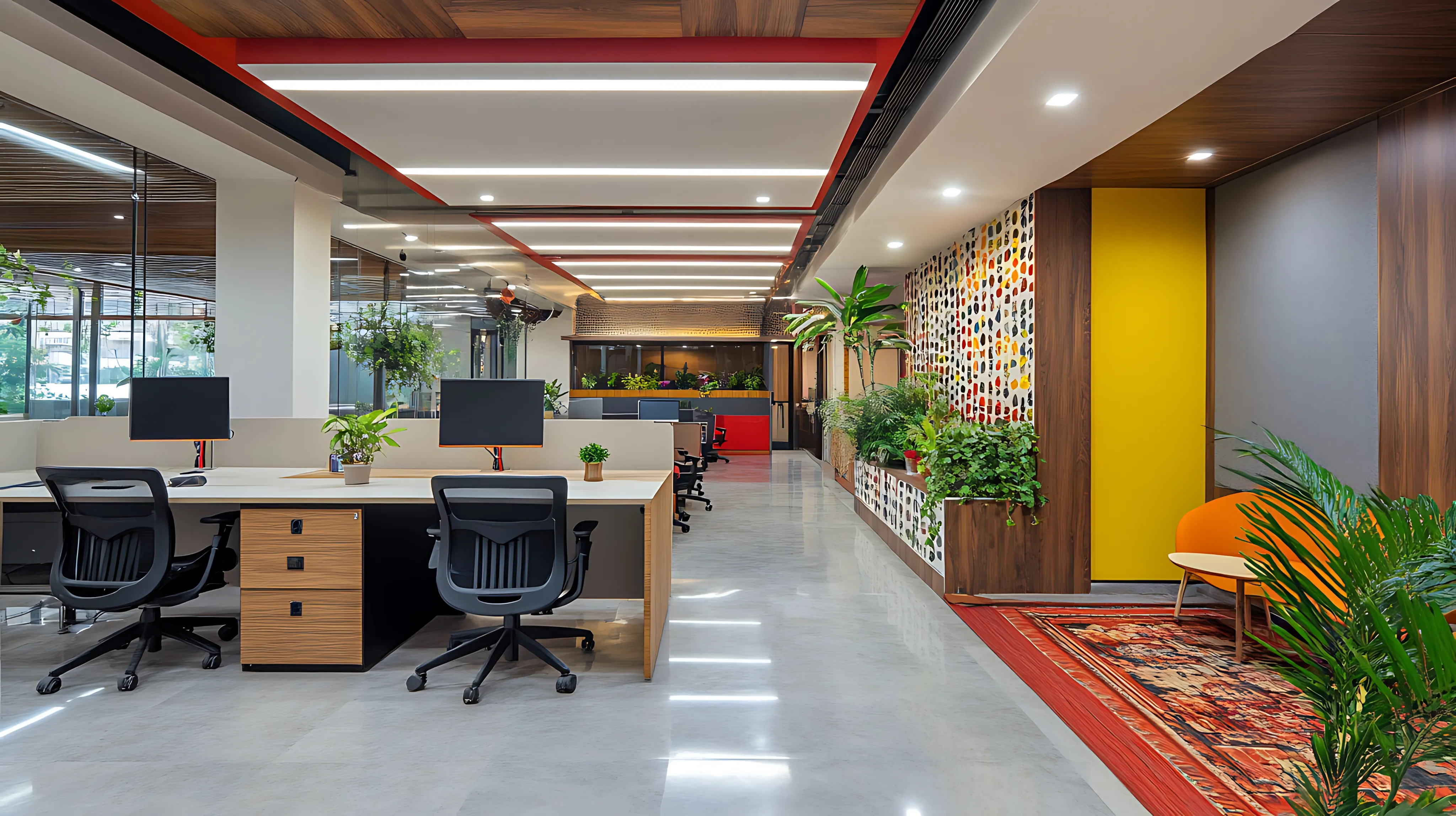 A long view of a modern, open-plan office workspace featuring rows of desks with computer monitors, vibrant yellow accents, and lush indoor plants under a stylish paneled ceiling.
