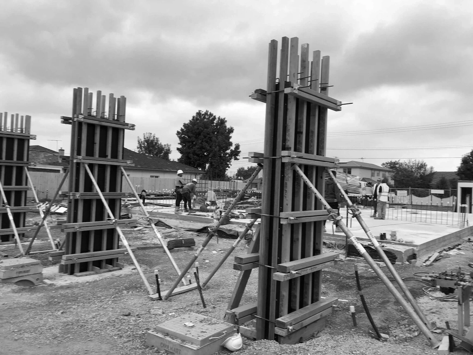 bw_image shows formwork for cocrete columns being held with orange timber and metal props with workers in the background