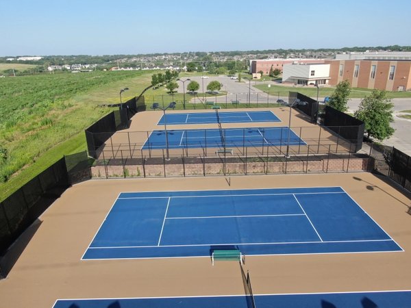 Aerial view of a resurfaced tennis court complex with bright blue playing surfaces and tan surrounding areas.