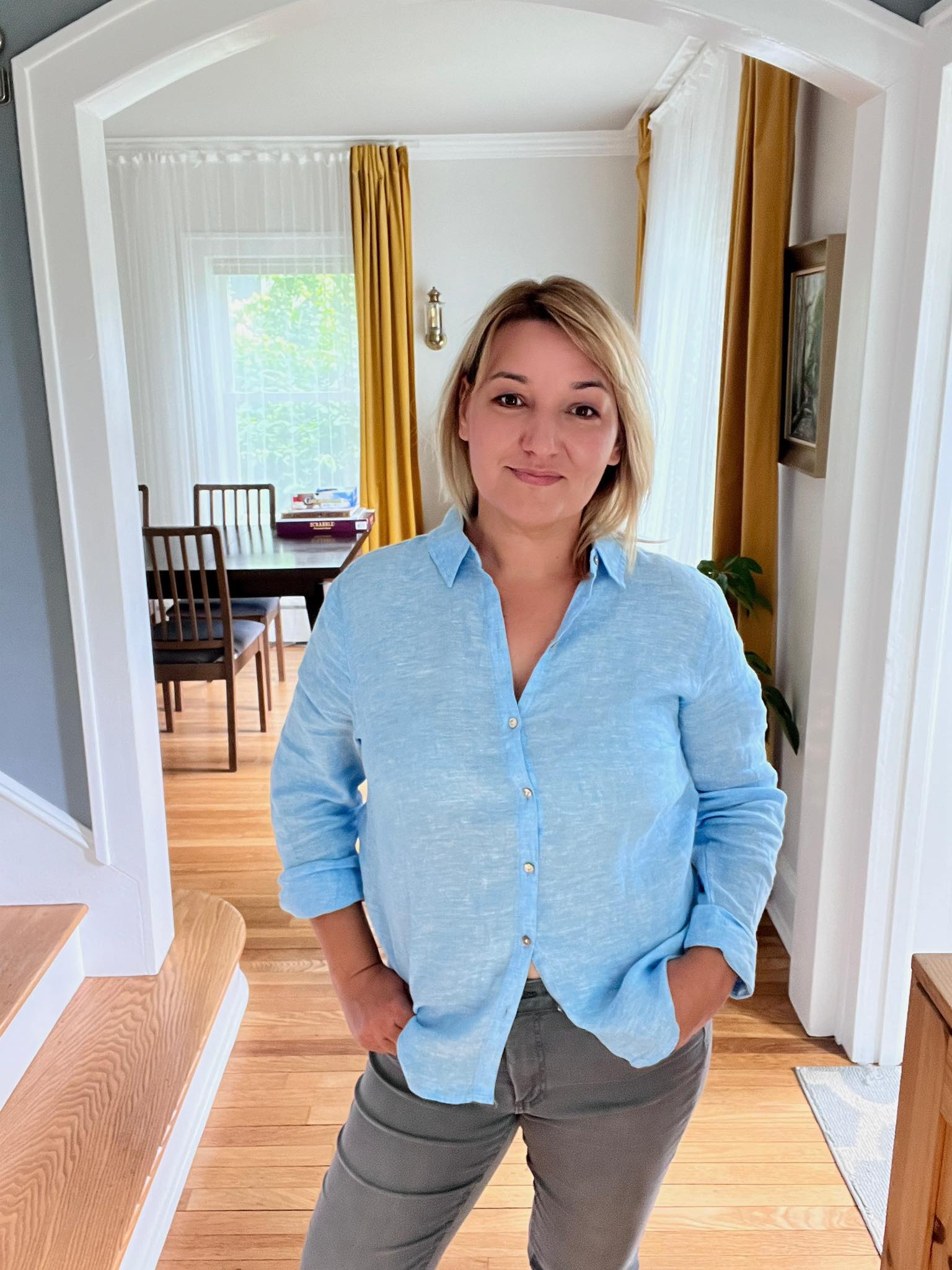 Smiling young woman with long hair standing against a dark green background, holding a finger to her chin.