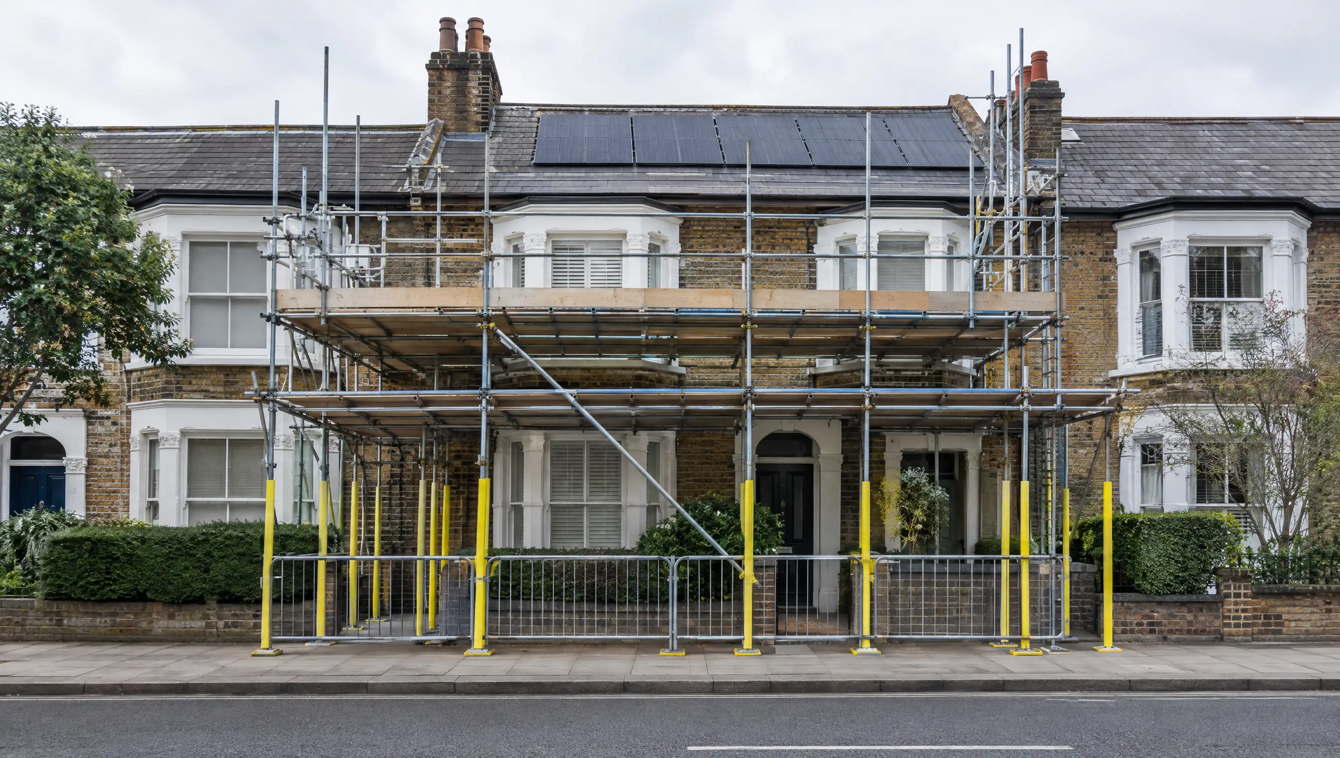 Scaffold with a covered pedestrian walkway on the pavement outside a London terraced house with solar panels