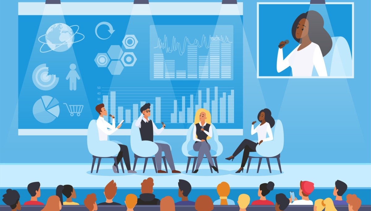 Photo of a panel discussion with four speakers on stage and data visuals on a large screen.