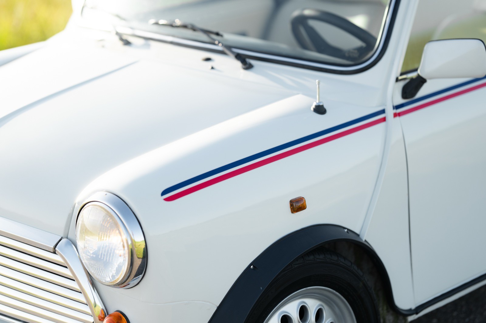 A close-up of a white car with a purple stripe, showcasing its round headlights and classic design.