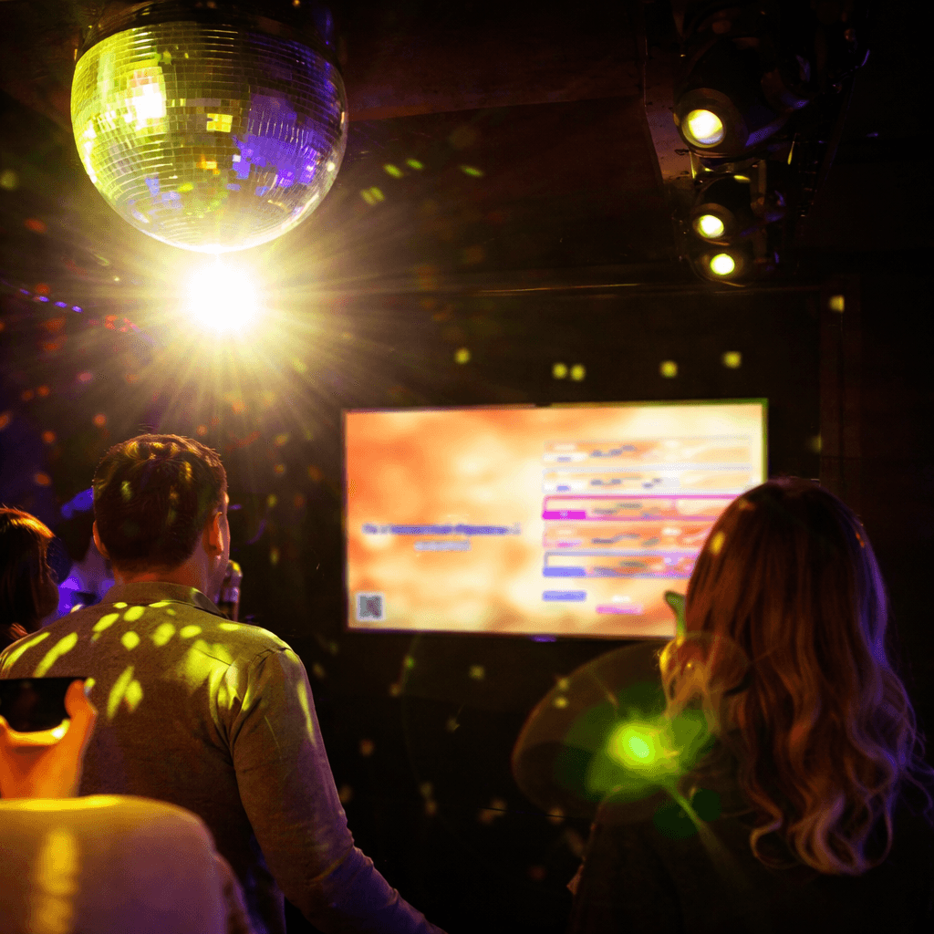 A young person with curly hair smiles at the camera while sitting in front of a laptop against a dark background.