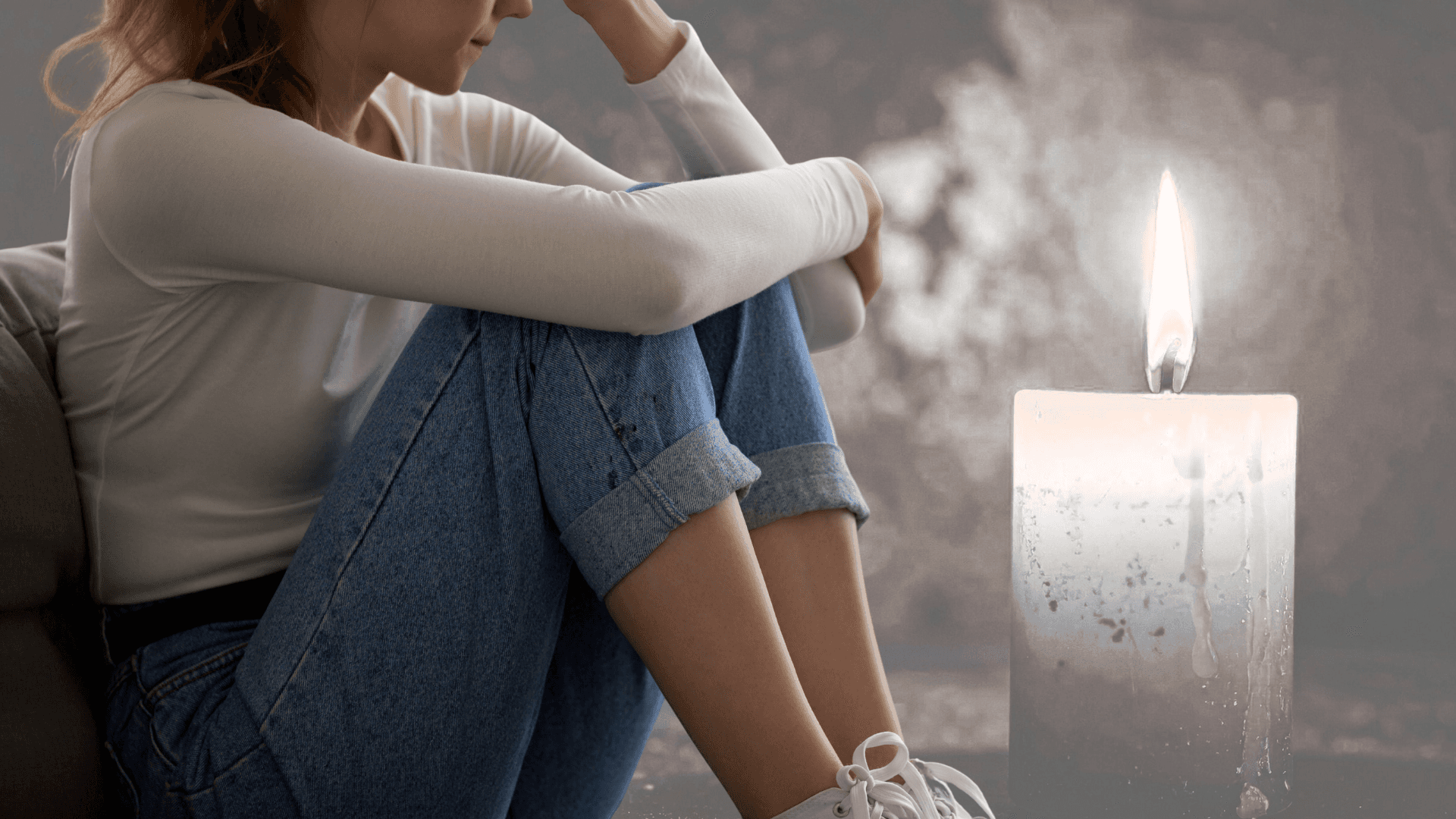 Oseba v tišini sedi ob sveči in razmišlja – simbol žalovanja in notranje bolečine.