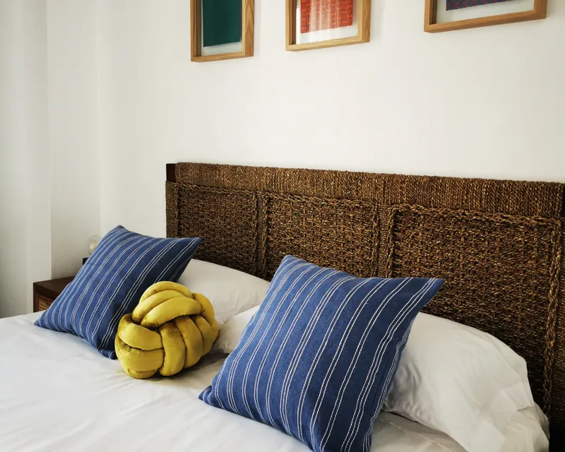 Detailaufnahme des Bettes im La Hipotenusa Tarifa – gestreifte Kissen treffen auf ein rustikales Kopfteil.