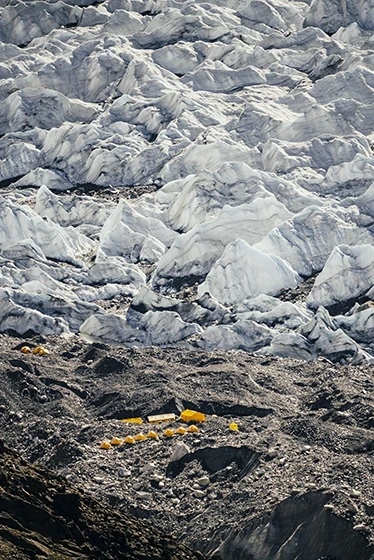 Obozowisko z żółtymi namiotami u podnóża lodowca w wysokich górach, kontrastujące z surowym, kamienistym terenem