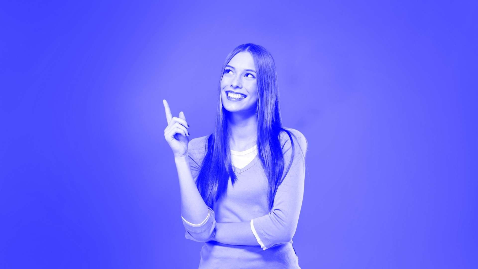 A smiling woman thinking with long hair, one arm folded across her waist and the other bent upwards at the elbow with a finger pointing upwards