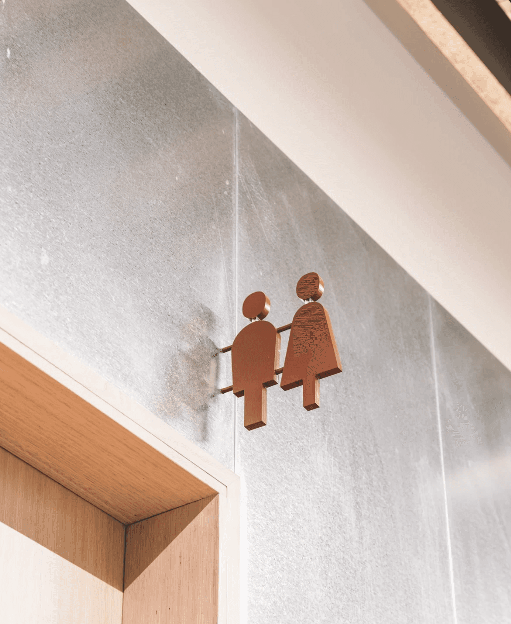 Custom terracotta dimensional restroom wayfinding sign with male and female figures, stud-mounted above a light oak doorway