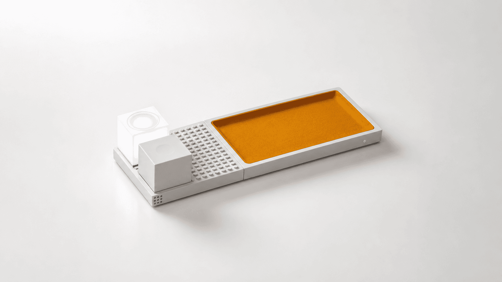 A clean studio product shot of the GridsLab modular wireless charging prototype with a LEGO-inspired platform, ambient light module, cube module, and orange wireless charging tray.