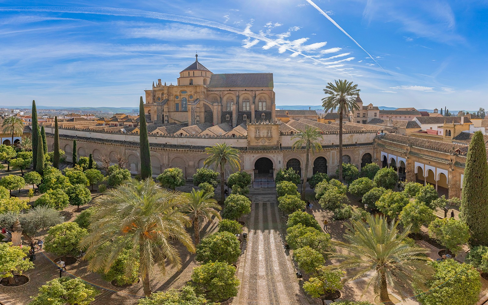 Die äußere Fassade der Mezquita-Catedral von Cordoba mit Gärten und Palmen unter einem blauen Himmel.