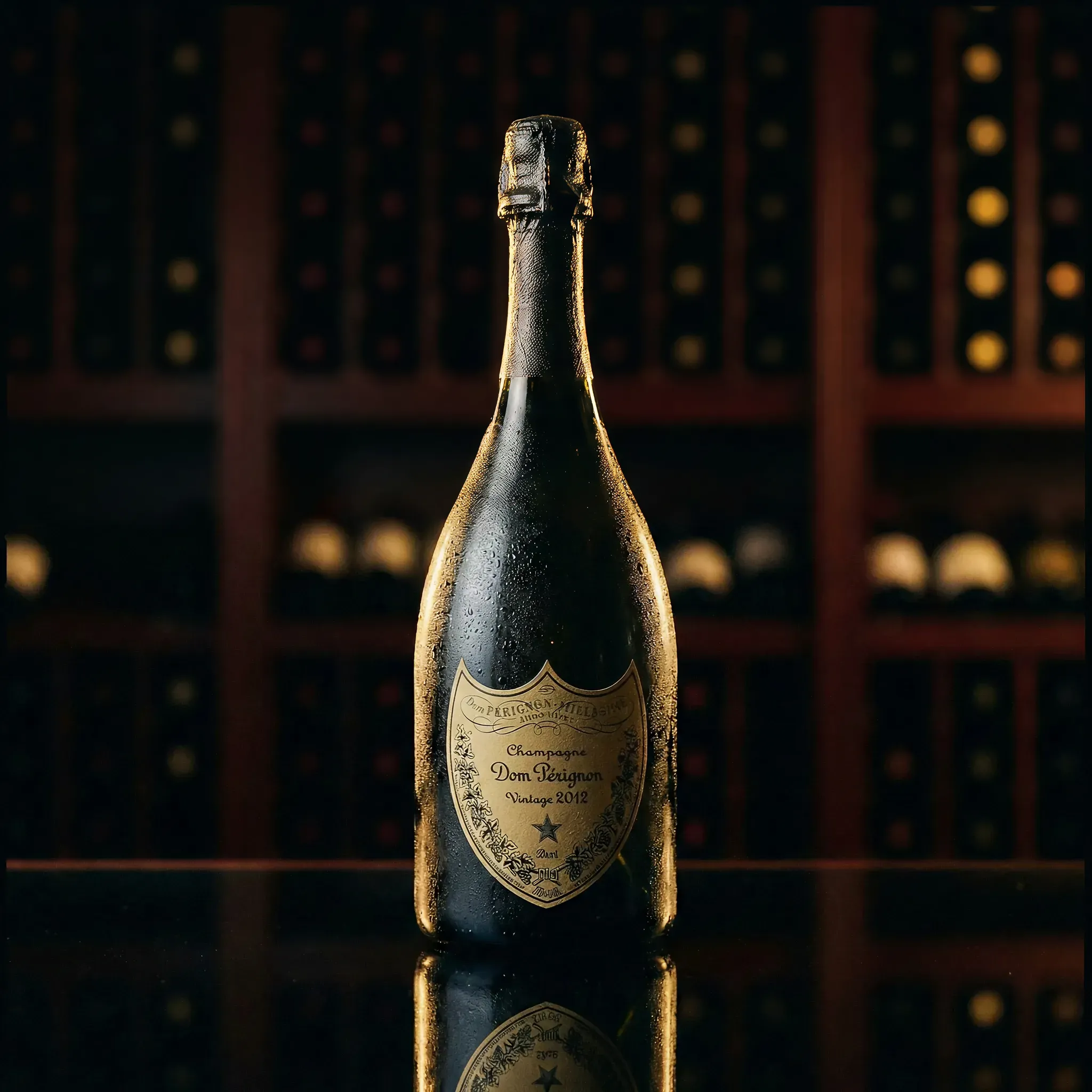 A bottle of Dom Pérignon Vintage 2012 champagne sits on a reflective surface, with water droplets enhancing its elegance. Background shows blurred wine racks.
