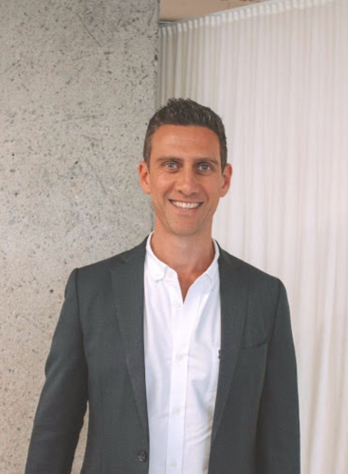 Man in dark suit jacket and white shirt smiles.