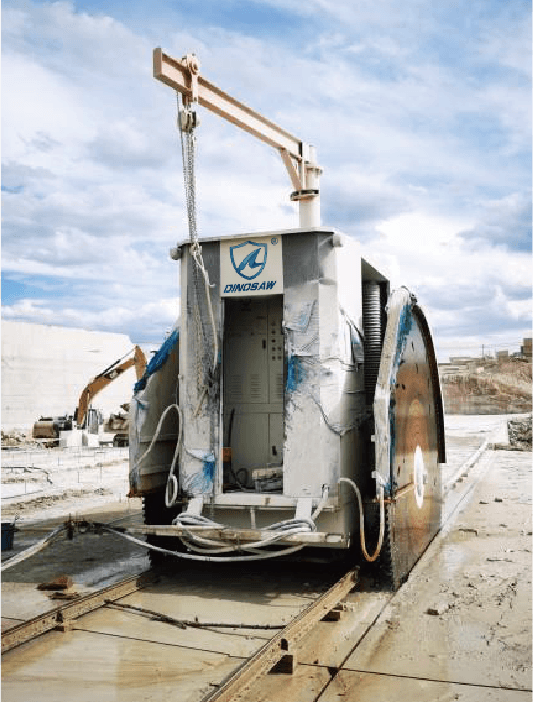 Rear view of the Double Blade Cutter Stone Quarrying Machine positioned on quarry tracks, illustrating its mobility and adaptability in various quarrying conditions with a cloudy sky in the background.