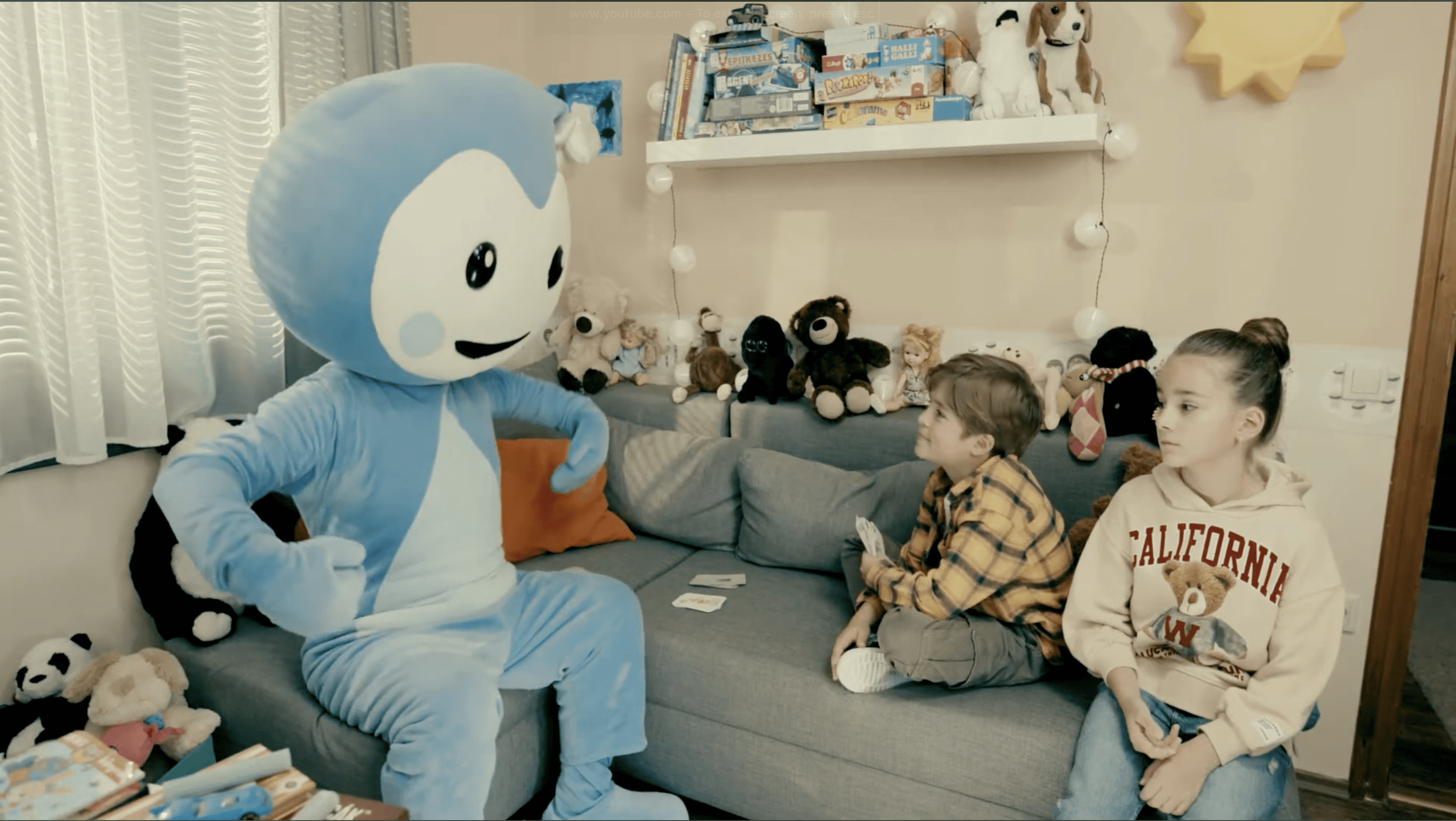 Cseppbarát kék kabalafigurája énekel a gyerekeknek a nappaliban.