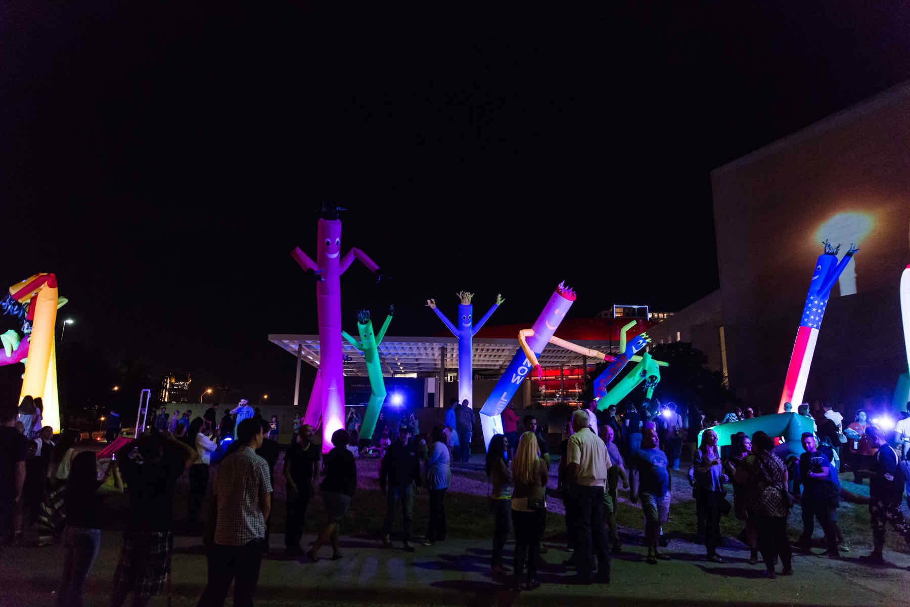 Vibrant, illuminated inflatables and colorful lights at a nighttime outdoor event with a crowd gathered.