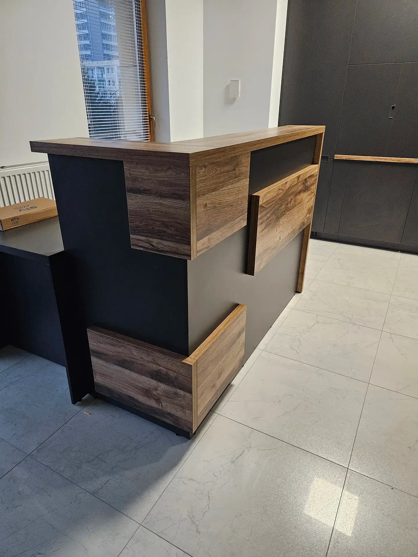 Elegancka lada recepcyjna o nowoczesnej bryle, wykonana z czarnej płyty i drewna.