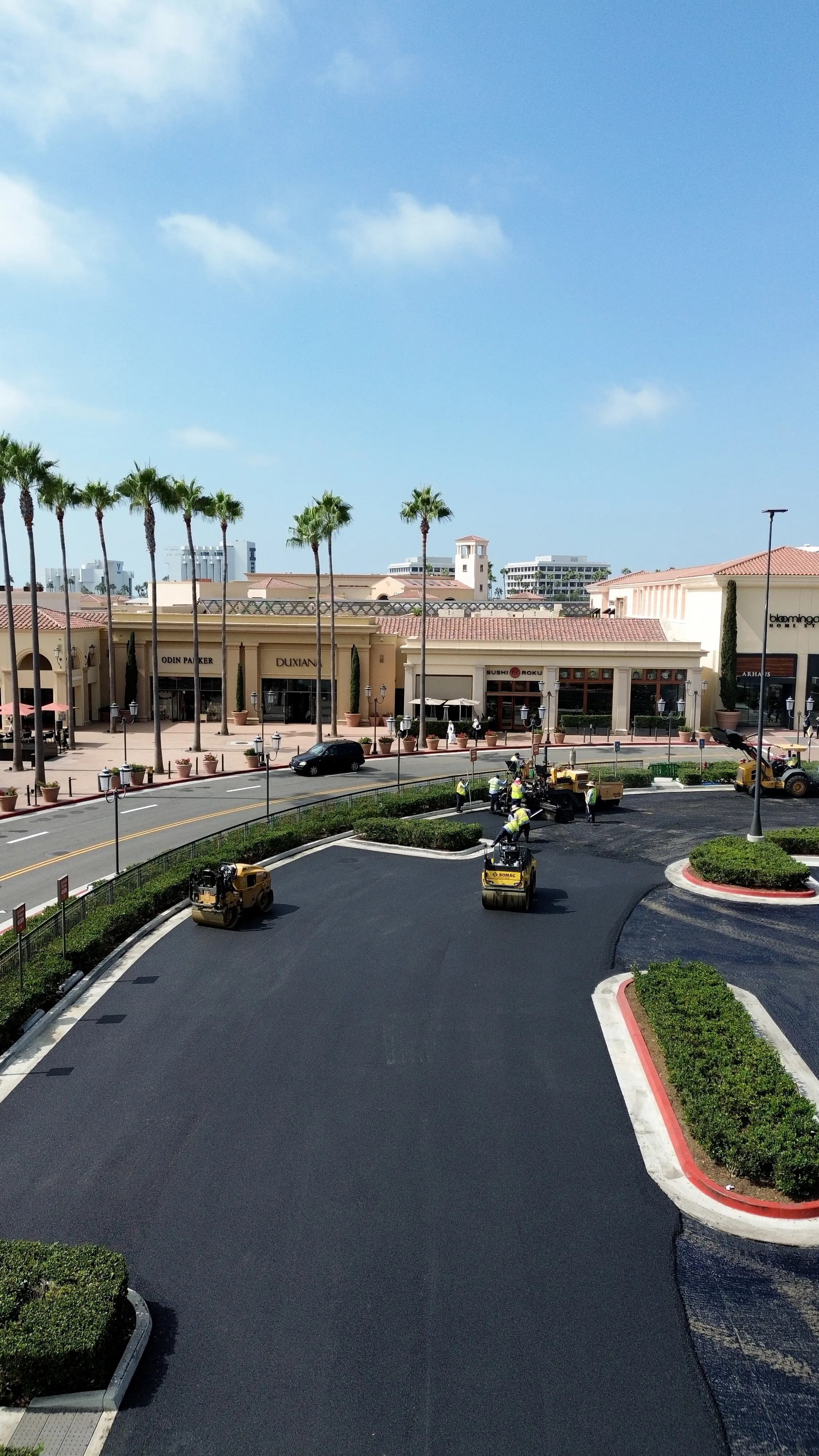 Aerial drone photo of rollers compacting new asphalt pavement at shopping center project