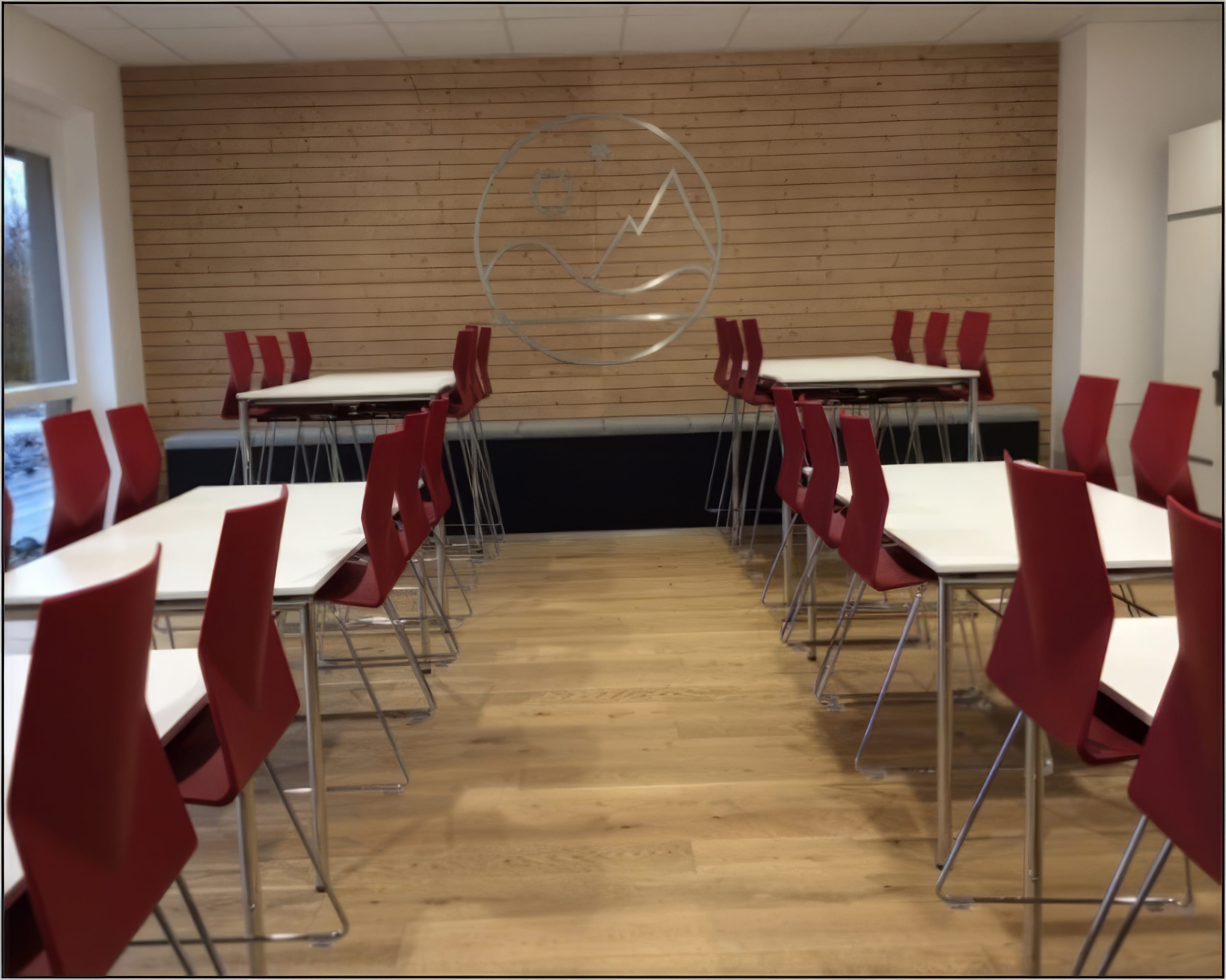 MW Interior  - Seminarraum mit weißen Tischen, roten Freischwingerstühlen, Eichenparkett und Holzwand mit eingelassenem Firmenlogo" Beschreibung: Einladender Seminar- und Pausenraum mit weißen Klapptischen, roten Schalenstühlen auf Chromgestell und einer markanten Holzwand mit eingelassenem Unternehmenslogo – Markenidentität und Raumgestaltung als Einheit.