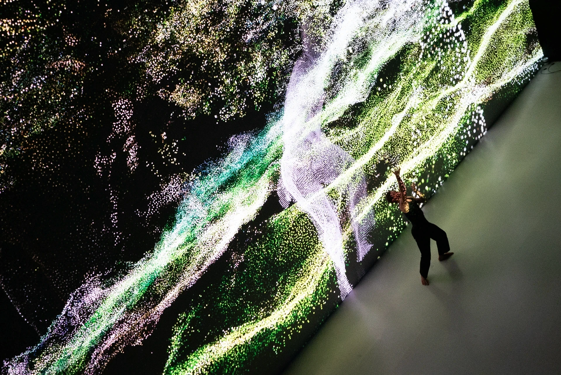 Dancer in front of a vibrant, particle-filled light installation.