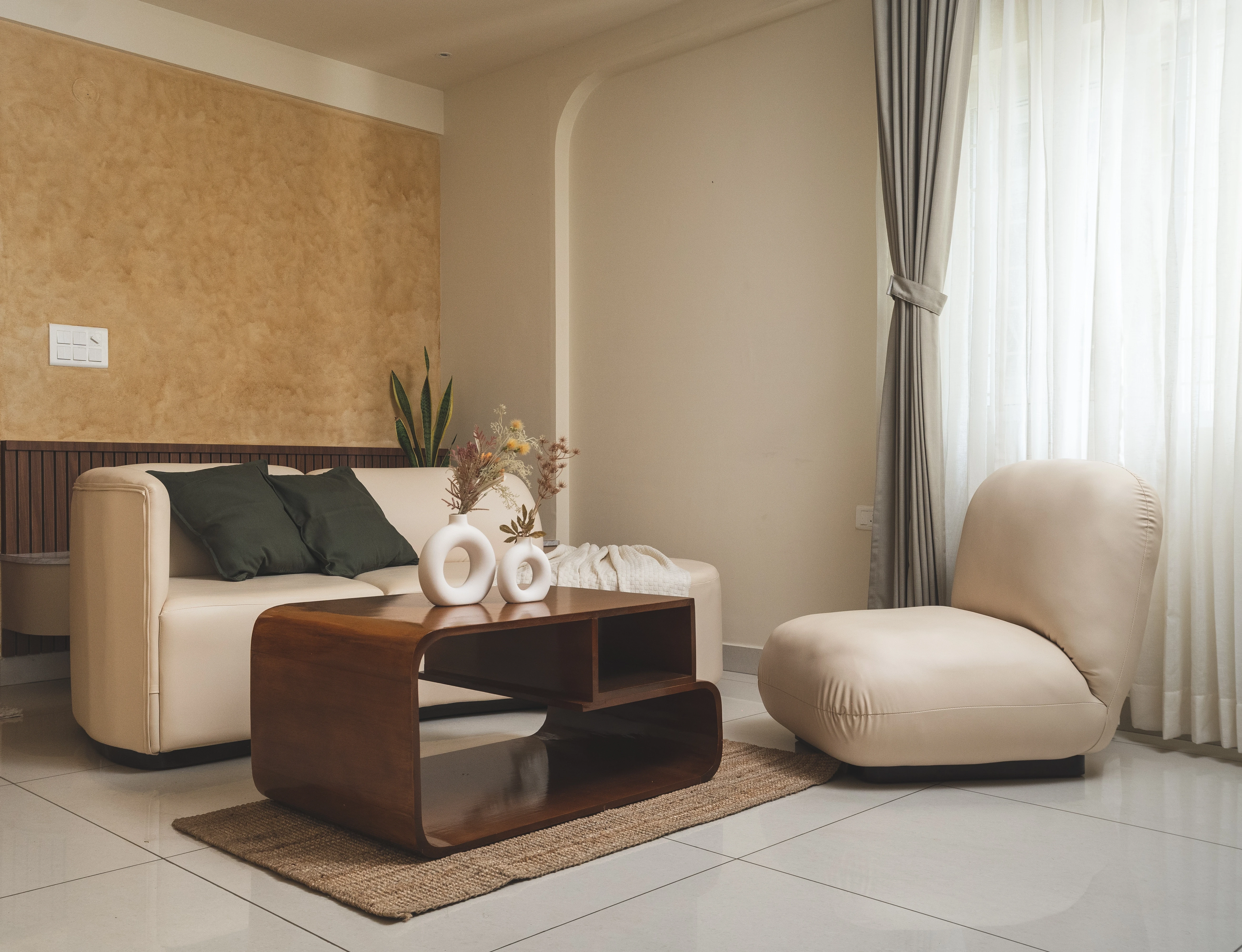 A modern living room showcasing a curved couch, coffee table, and chair, inspired by Japanese minimalism and South Indian aesthetics.
