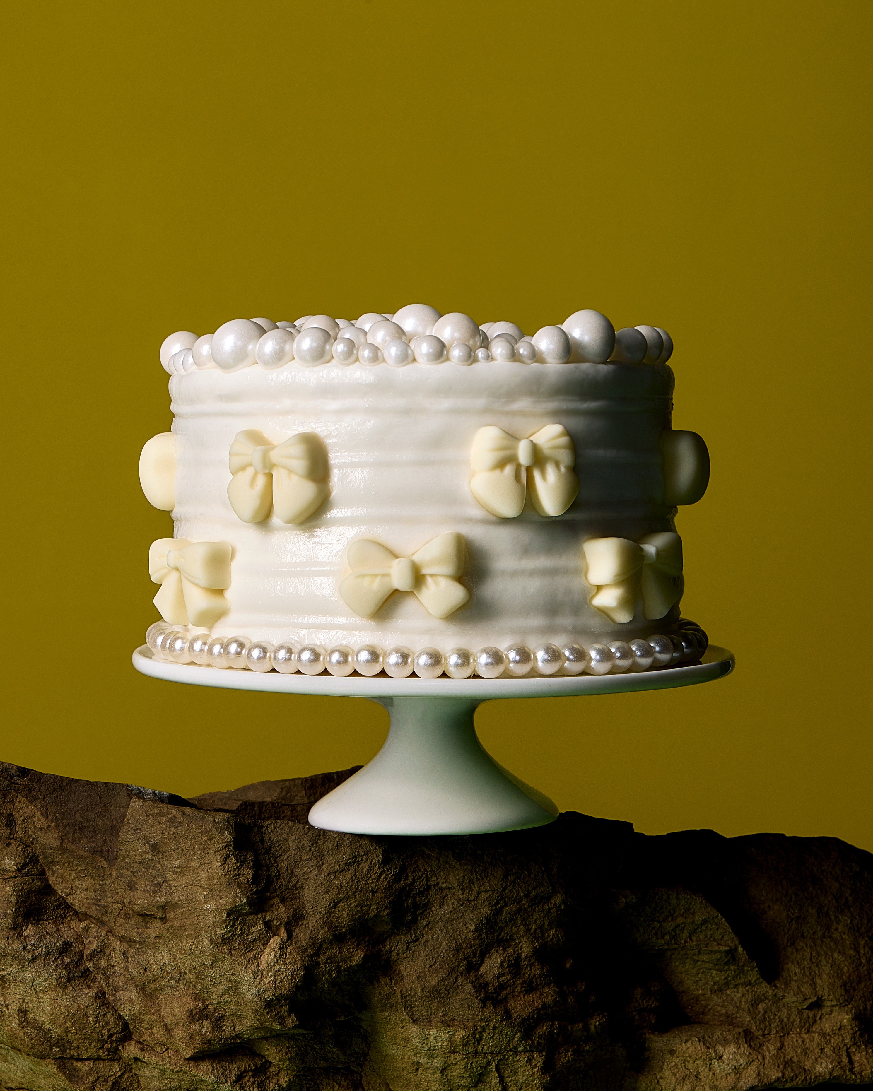 White pearl and bow cake on a pedestal against a yellow background