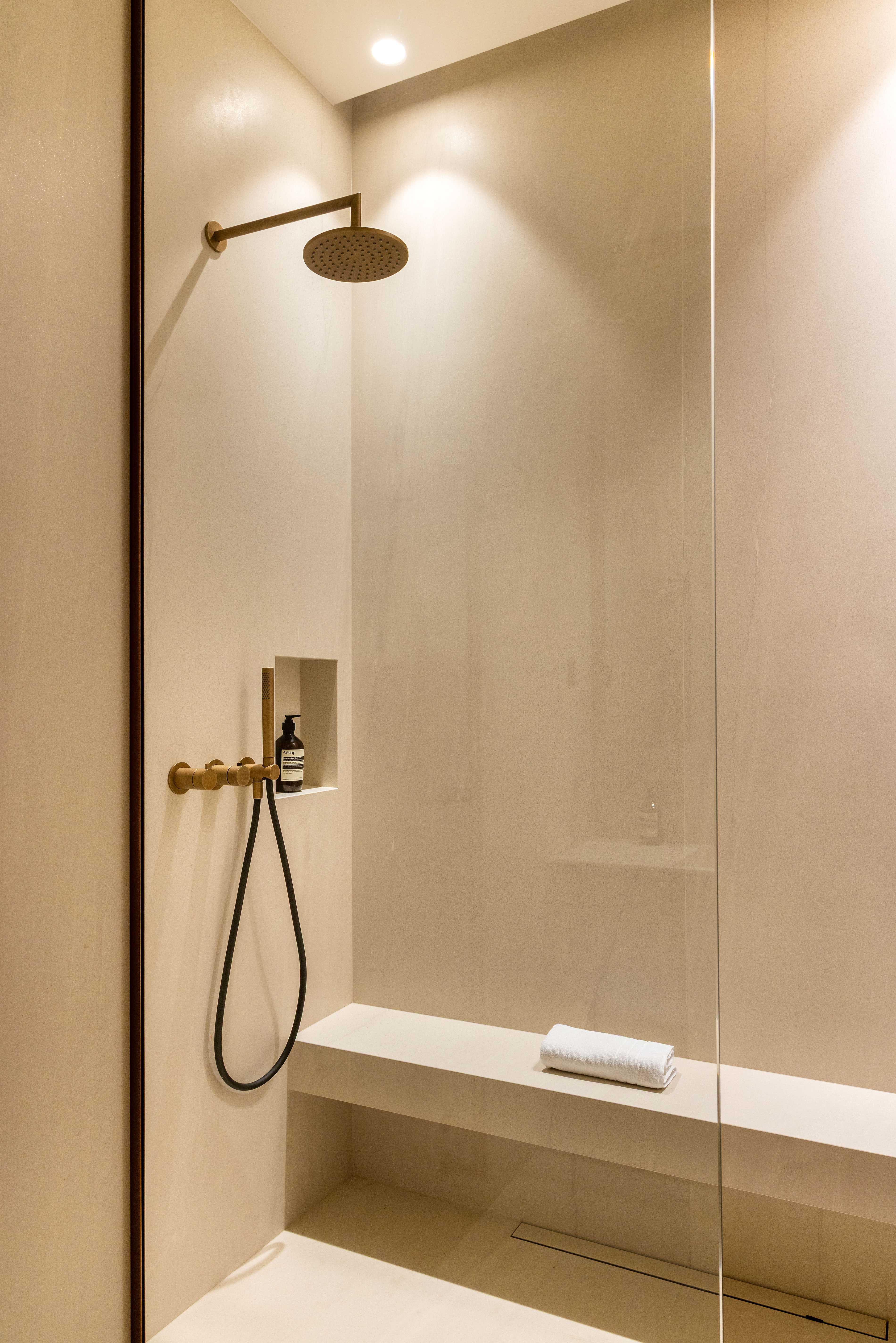 Douche italienne spacieuse avec pommeau doré, banc en pierre, niche et paroi vitrée