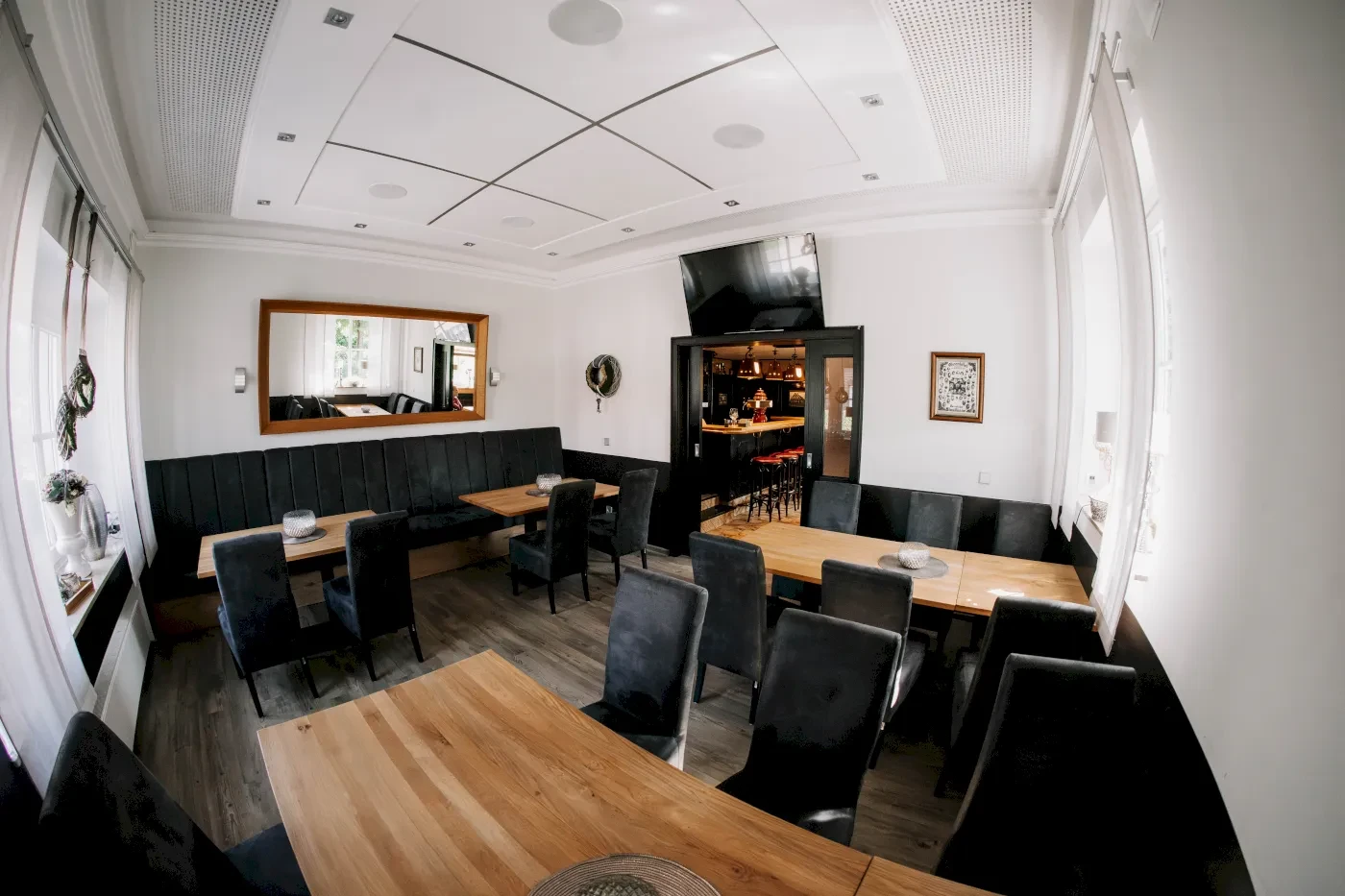 Einladender Innenraum mit Tischen, Stühlen, Spiegel und einem Fernseher an der Wand. Holzmöbel und dunkle Sitzmöglichkeiten.