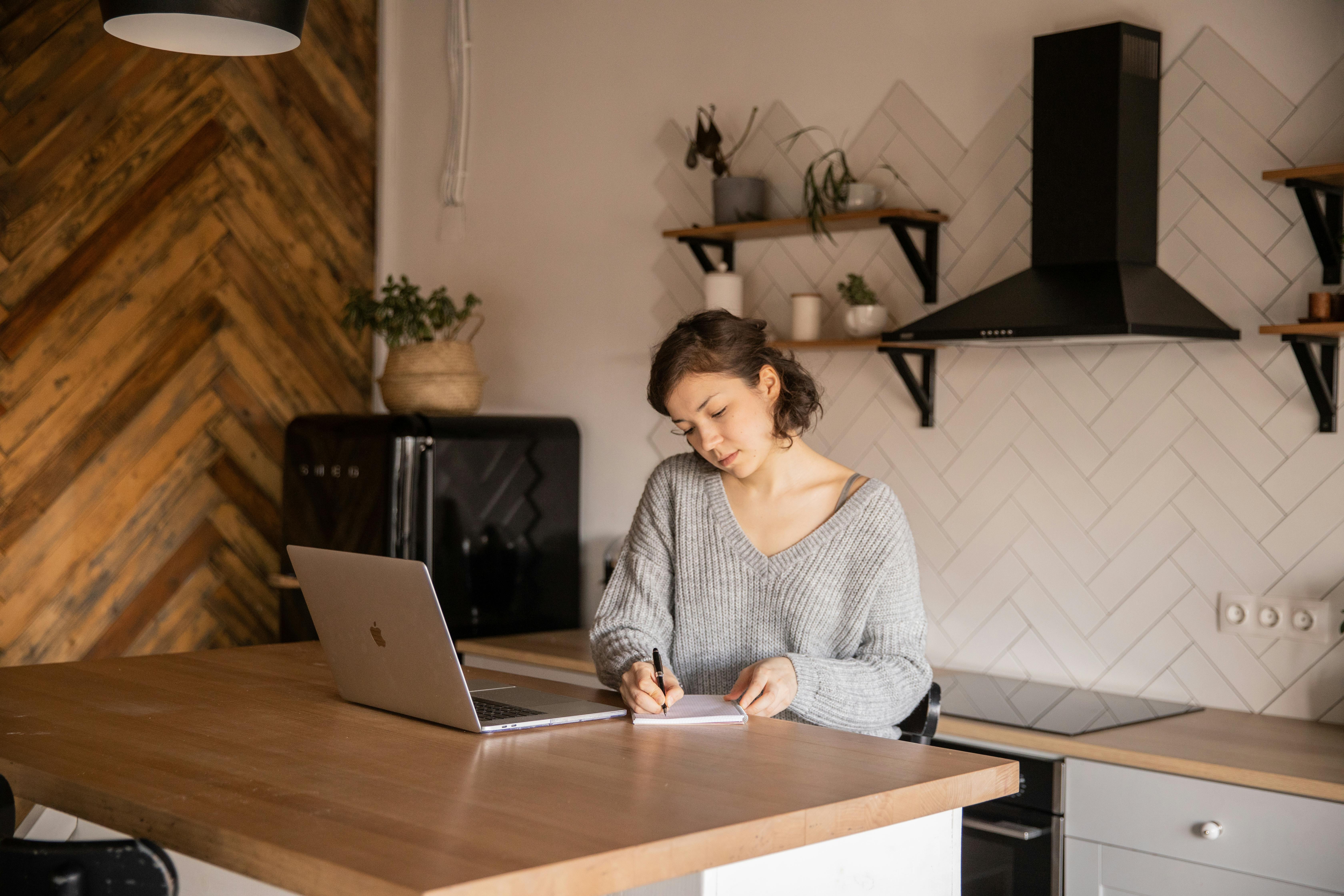 Woman taking out a loan with laptop and notepad in kitchen