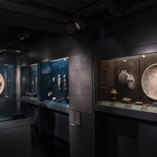 灯光昏暗的博物馆展区内,古代文物和陶器陈列在带有说明牌的玻璃展柜中。