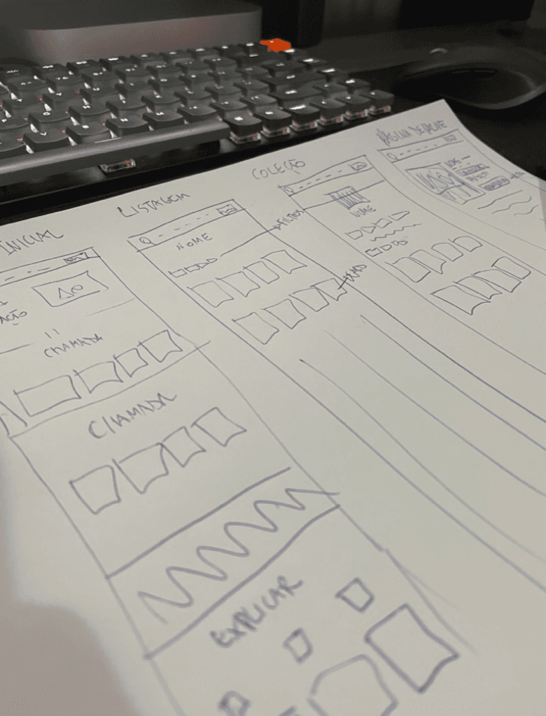 Folhas com esboços de interface desenhados à mão sobre uma mesa, ao lado de um teclado mecânico.