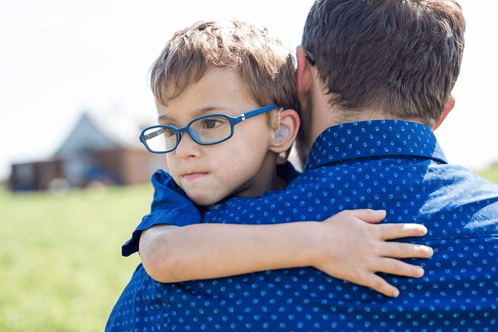 Child with hearing aid hugging man