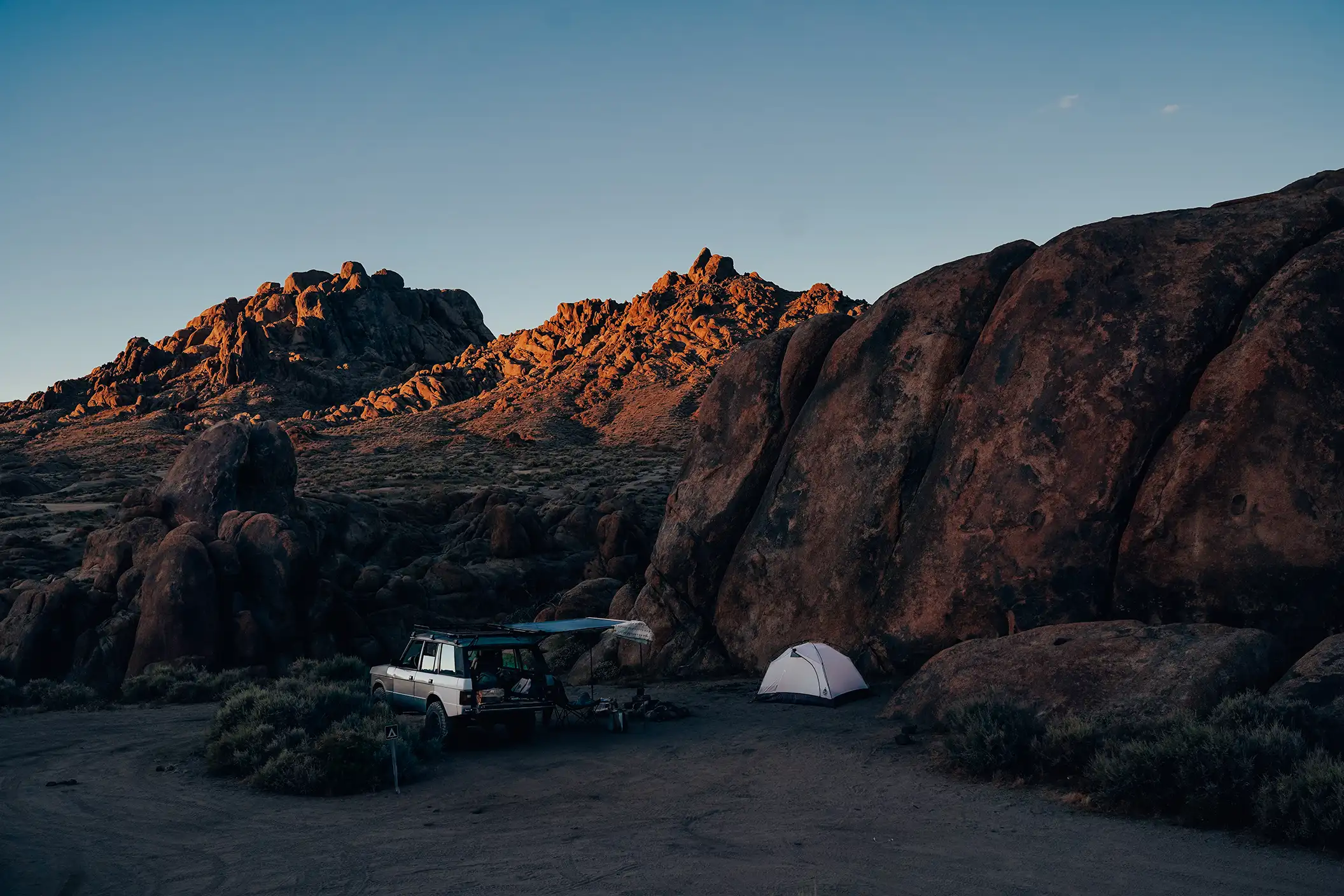 A silver Range Rover SUV parked next to a tent at dusk.