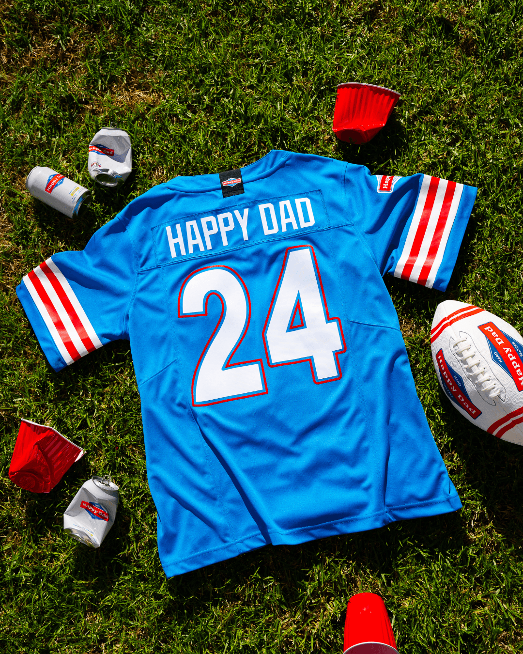 A blue sports jersey with number 24 is laid on grass, surrounded by red cups and two footballs.