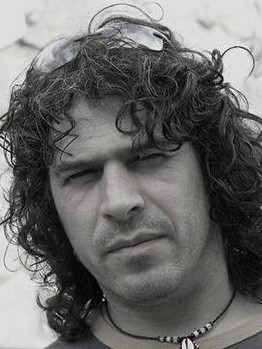 Retrato blanco y negro de hombre con pelo largo negro rizado y un collar con concha