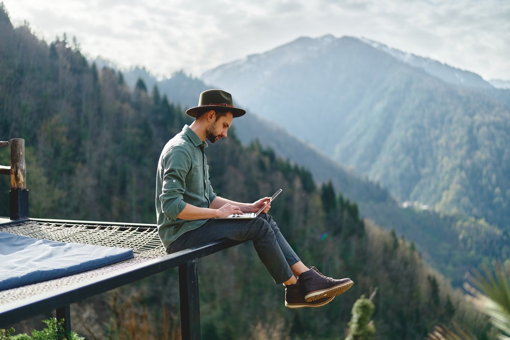 Ragazzo lavora sul pc portatile circondato da montagne 