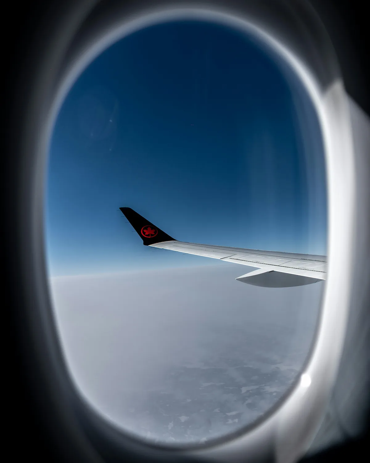 A view of the wing of an airplane with a red maple leaf on it in the sky