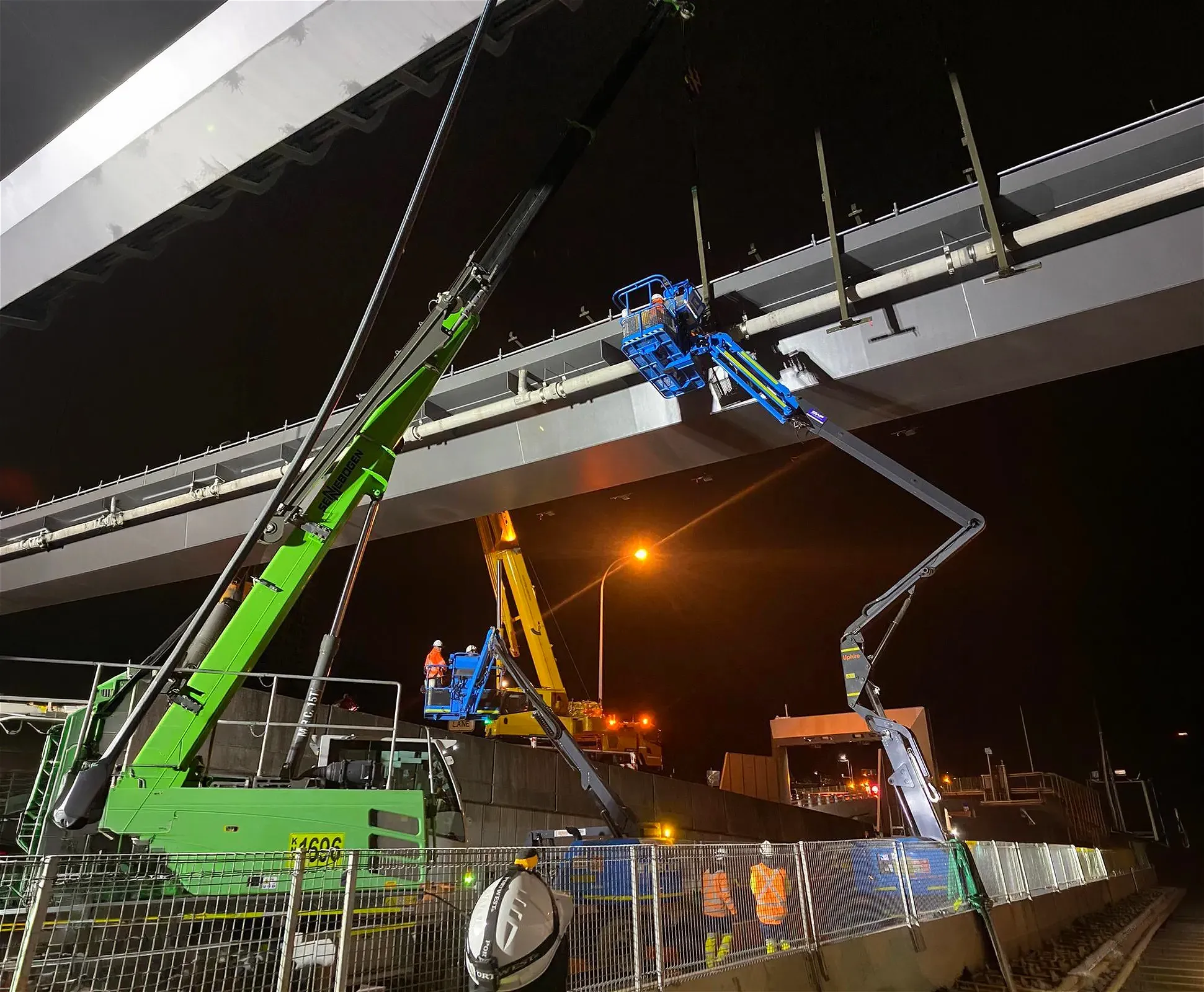 Construction crew working on bridge at night with cranes and lifts.