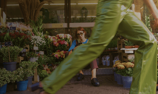 Eine Person geht zügig an einem lebhaften Blumenstand vorbei, der mit einer Vielzahl bunter Blüten und Topfpflanzen gefüllt ist.
