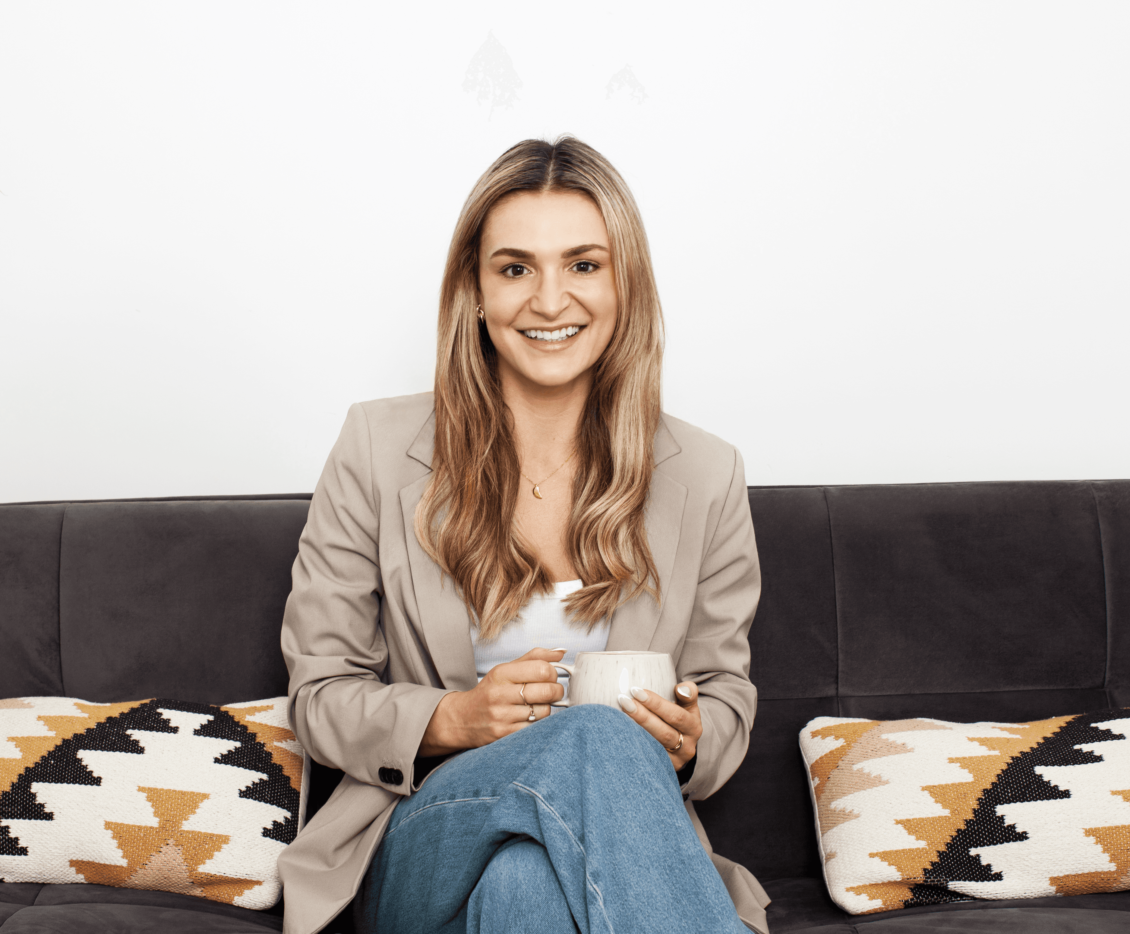 Woman sitting on a sofa holding a mug, smiling in a bright, comfortable living room.