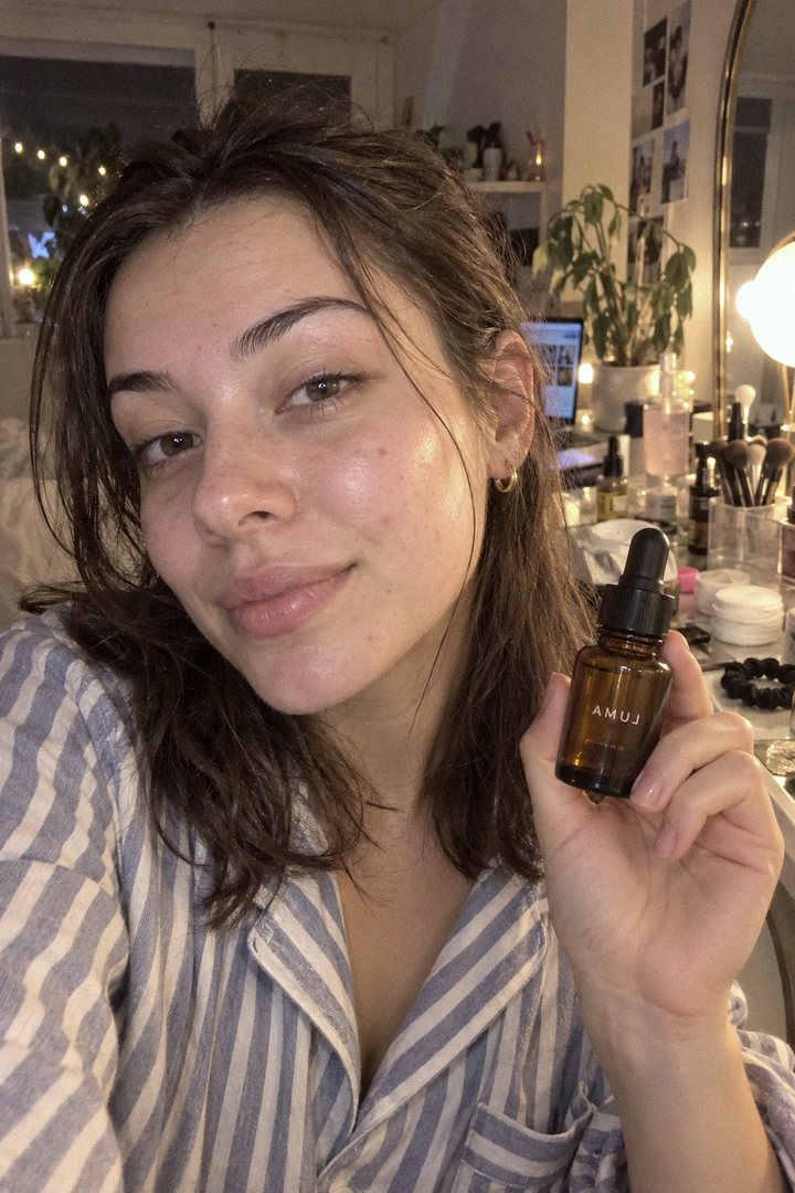 Option C: a creator holding a dropper bottle beside her face at her vanity