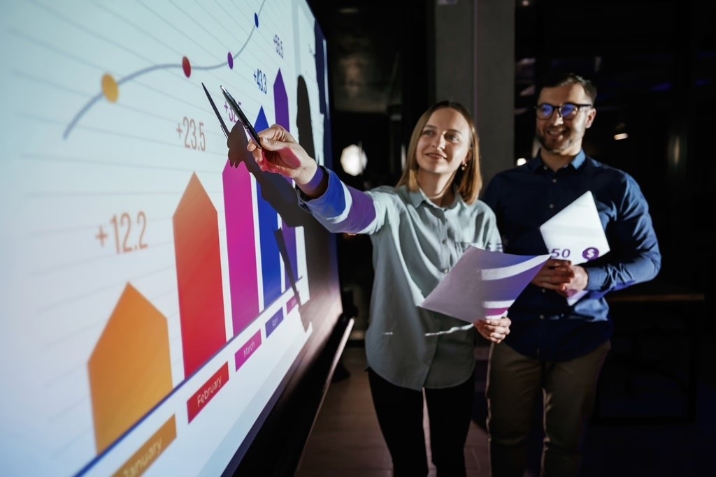 Man presenting charts on a large screen to audience.